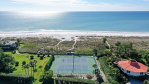 Un campo da tennis circondato da vegetazione rigogliosa e vista sulla spiaggia.