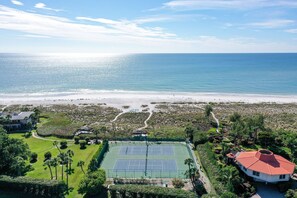 Uma quadra de tênis cercada por vegetação exuberante e vista para a praia.