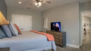 Ein Schlafzimmer mit einem Bett, Kissen, einem Fernseher, einem Deckenventilator und einer Kommode.