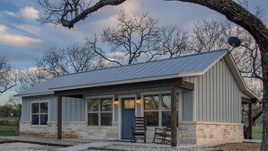 Eine rustikale Holzhütte mit einem Metalldach, einem Steinfundament und einer Veranda mit zwei Holzstühlen.