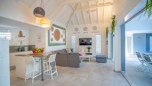 A modern kitchen with white cabinetry, a dining area with a grey sofa, and a TV mounted on the wall.