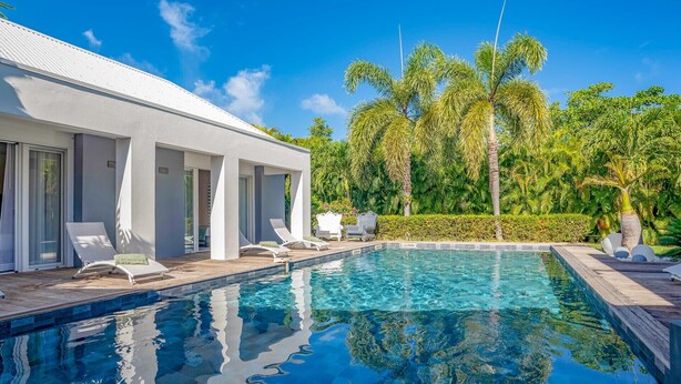 A modern pool area with clear blue water, lounge chairs, and a white building with large windows.