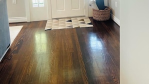 A hallway with a wooden floor, a white door with glass panels, and a basket with a blue cushion.