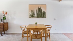 Un'area pranzo con un tavolo di legno e quattro sedie, un vaso con una pianta e un quadro raffigurante un cactus al muro.