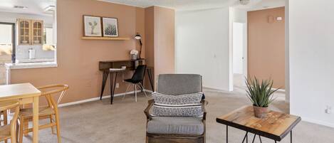 Een ruime woonkamer met een eethoek, een grijze fauteuil, een houten salontafel en een plant in pot.