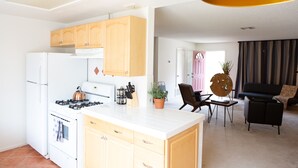 Una cucina moderna con mobili in legno, piano cottura bianco e angolo pranzo con divano nero e tavolo.