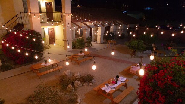 Un'area patio esterna con luci decorative, panche e tavoli in legno.