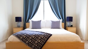 Un letto rifatto con una coperta a righe bianche e azzurre, due abat-jour e una vista attraverso tende leggere.