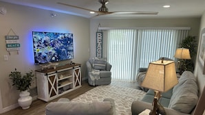 A living room with a television, two couches, a ceiling fan, and a large window with blinds. - Direct Gulf View, Beach Condo on Manasota Key, FL (Englewood)