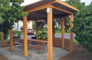 Un mirador de madera con techo, rodeado de follaje y una mesa de picnic.