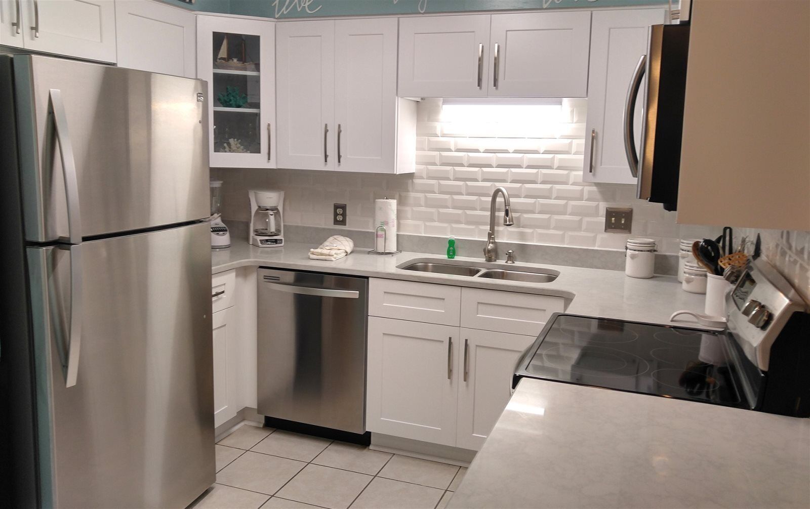 A modern kitchen with stainless steel appliances, white cabinetry, and a tiled backsplash.