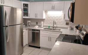 A modern kitchen with stainless steel appliances, white cabinetry, and a tiled backsplash. - Serene #202 Chateau La Mer II 1Bd-1Bath Ground Floor 2 Queen Beds &Sofabed (Destin)