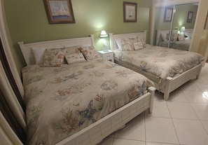 Un dormitorio con dos camas, una mesita de noche, una lámpara y un espejo.