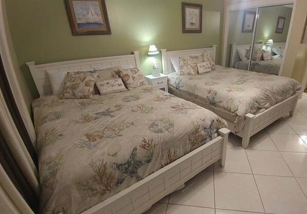 A bedroom with two beds, a nightstand, a lamp, and a mirror. - Serene #202 Chateau La Mer II 1Bd-1Bath Ground Floor 2 Queen Beds &Sofabed (Destin)