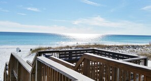 Una terraza de madera con vista a una playa, bajo un cielo despejado.