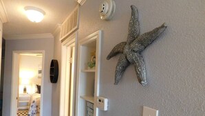 Ein Flur mit einer Meerstern-Dekoration, einer Deckenleuchte und einer Tür zu einem Zimmer mit einem Bett und einem Nachttisch.