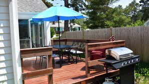 Un terrazzo in legno con un barbecue, un tavolo e sedie, e un ombrello blu.