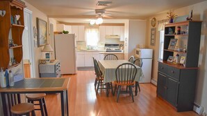 A compact kitchen with wooden cabinets, a dining table with chairs, and a refrigerator.