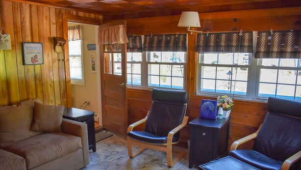 A cozy room with wooden walls, a sofa, two chairs, a small table, and a lamp.