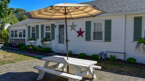 A white house with green shutters, a picnic table, and an umbrella.
