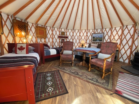 A cozy interior of a yurt with two beds, a dining table, and two chairs.
