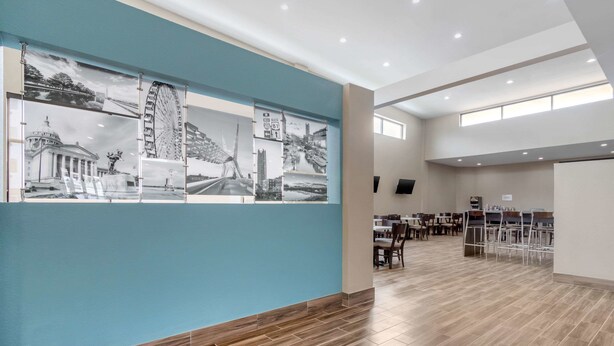 A spacious hotel lobby with a large wall mural, multiple dining tables, and a modern tiled floor.
