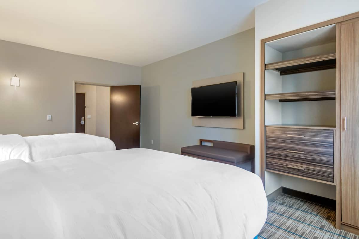 Een hotelkamer met twee bedden, een aan de muur bevestigde televisie, een houten garderobe en een bankje.