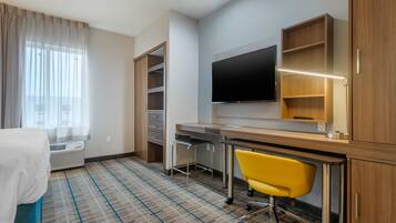Ein Hotelzimmer mit Bett, Schreibtisch, Stuhl, Fernseher und fest installierten Regalen.