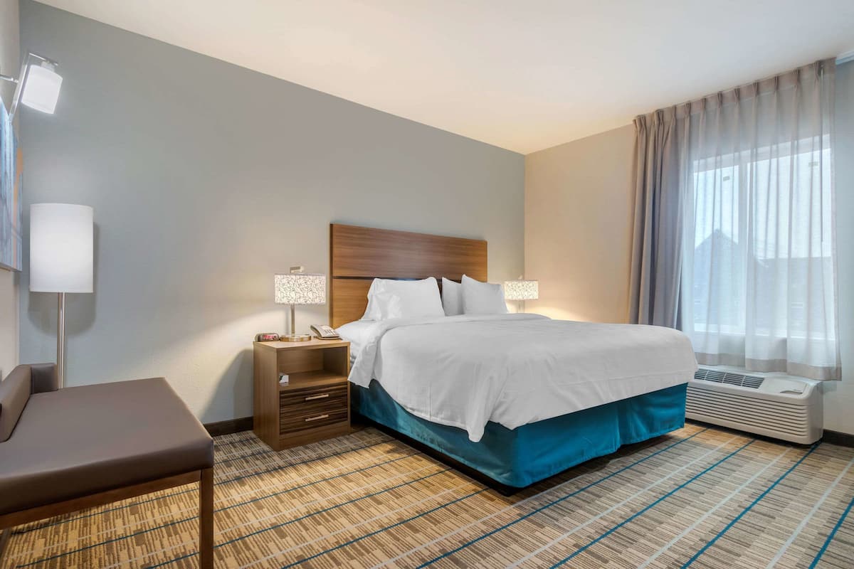 Een hotelkamer met een bed, nachtkastjes, een lamp, een stoel en een raam met gordijnen.