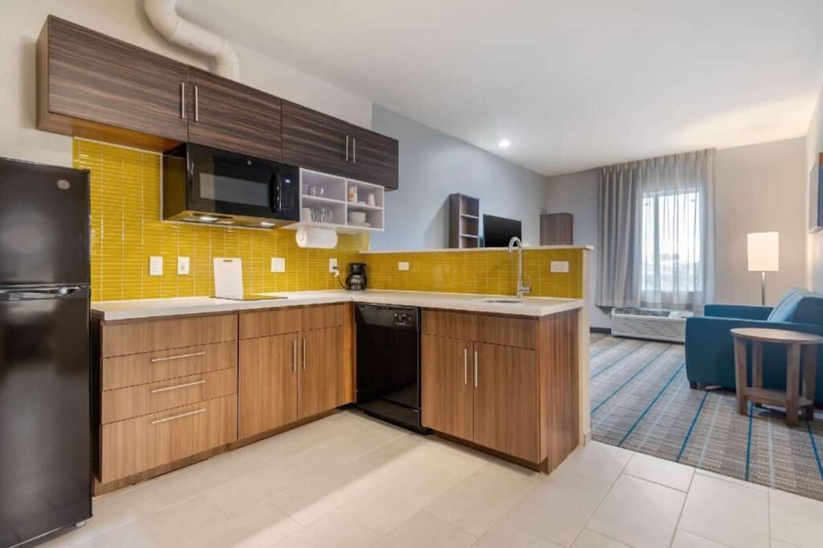Een moderne keuken met houten kastjes, een ingebouwde magnetron en een gele spatwand.