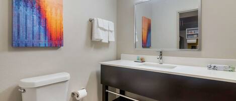 Un baño moderno con inodoro blanco, tocador oscuro, espejo grande y un cuadro abstracto de colores en la pared.