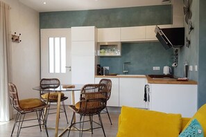 Une cuisine moderne avec des armoires blanches, un four à micro-ondes encastré et une hotte noire. On y trouve également un coin repas avec des chaises en osier et un coussin jaune.
