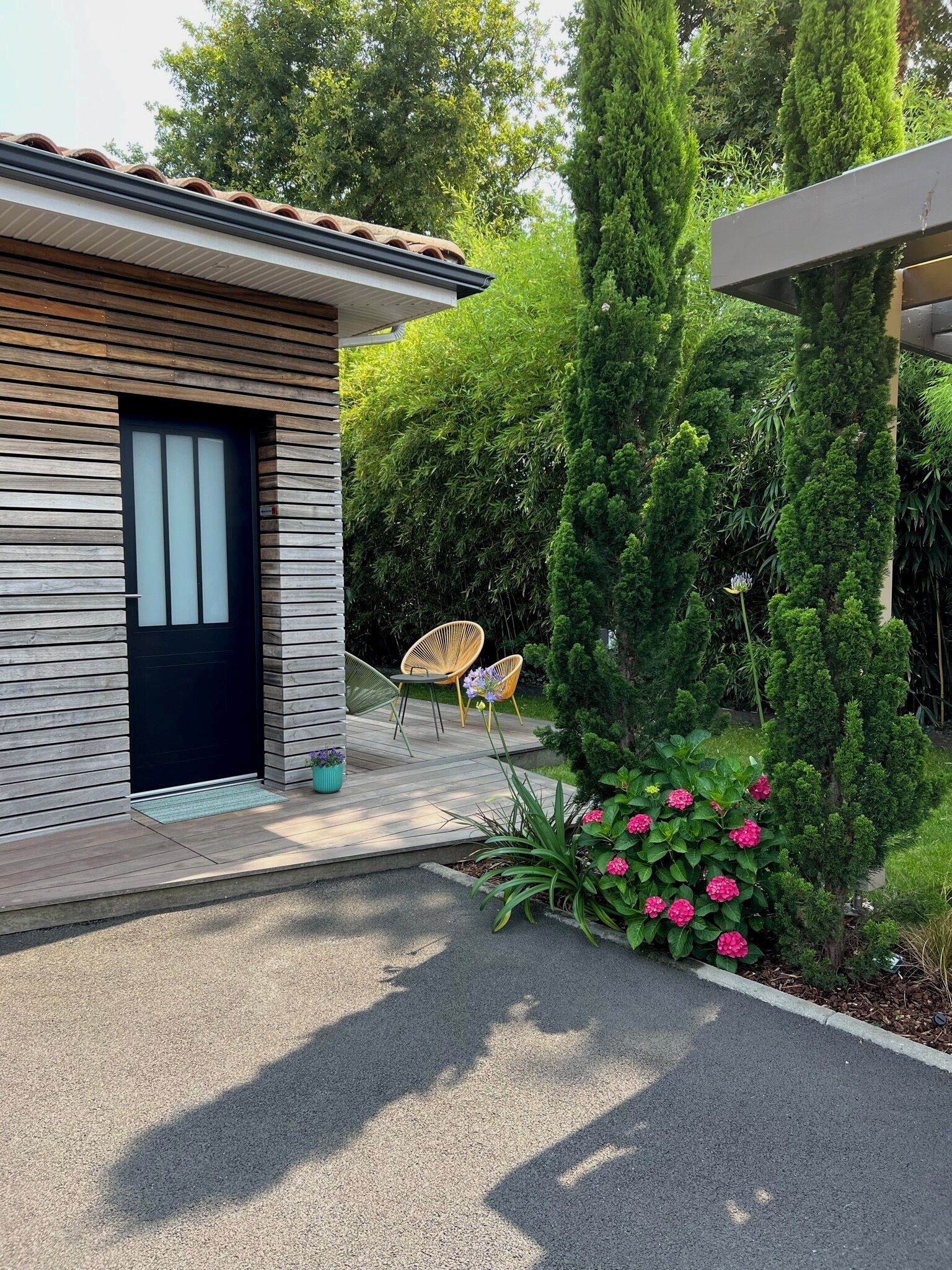 A modern house with a wooden exterior, a black door, and a small patio with two chairs and a table.
