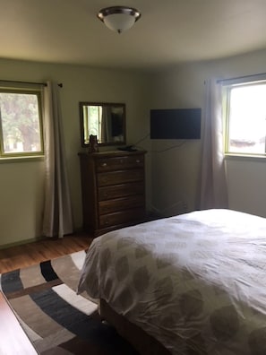 Un dormitorio con cama, cómoda y televisor montado en la pared.