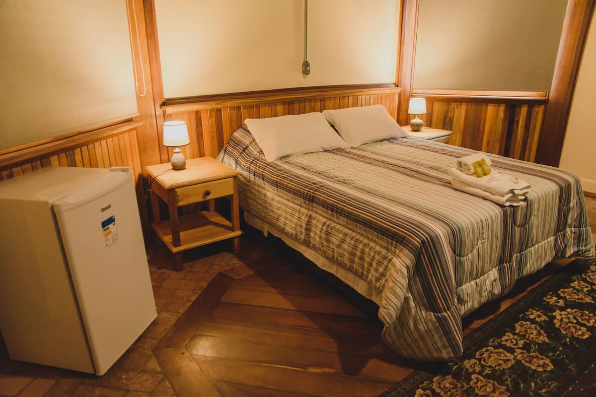 A hotel room with a bed, a nightstand, a lamp, and a refrigerator.