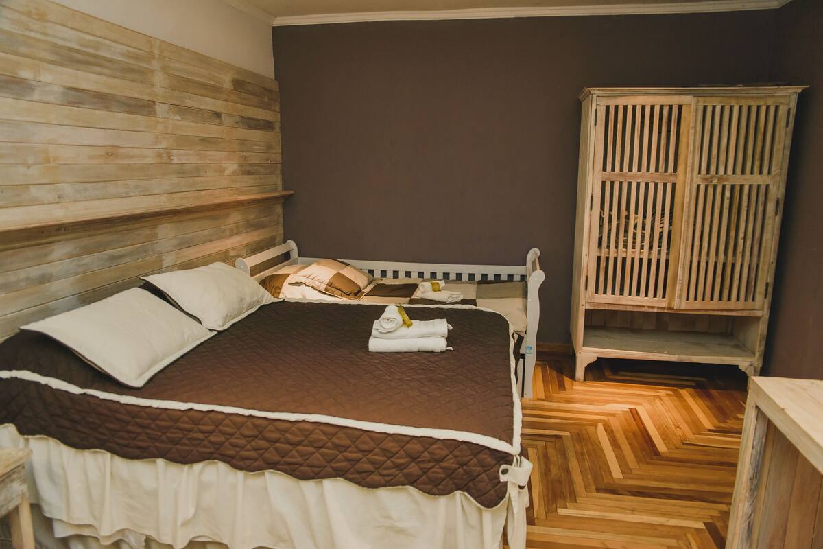 A bedroom with a wooden headboard, a bed with a quilted cover, and a wooden wardrobe.