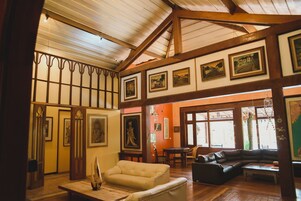 Ampla sala de estar com pé direito alto, vigas de madeira e várias obras de arte emolduradas nas paredes.