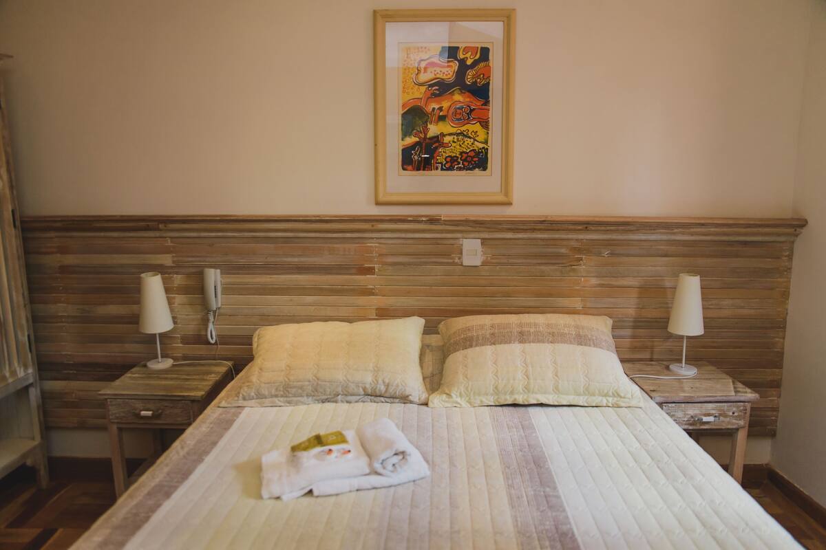 A neatly made bed with two pillows, a folded towel, and a framed picture on the wall.