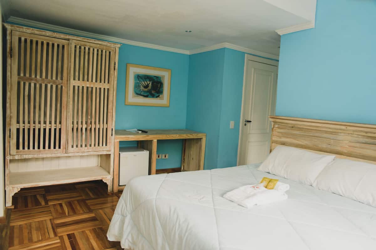 A bedroom with a bed, a wooden desk, a wardrobe, and a painting on the wall.