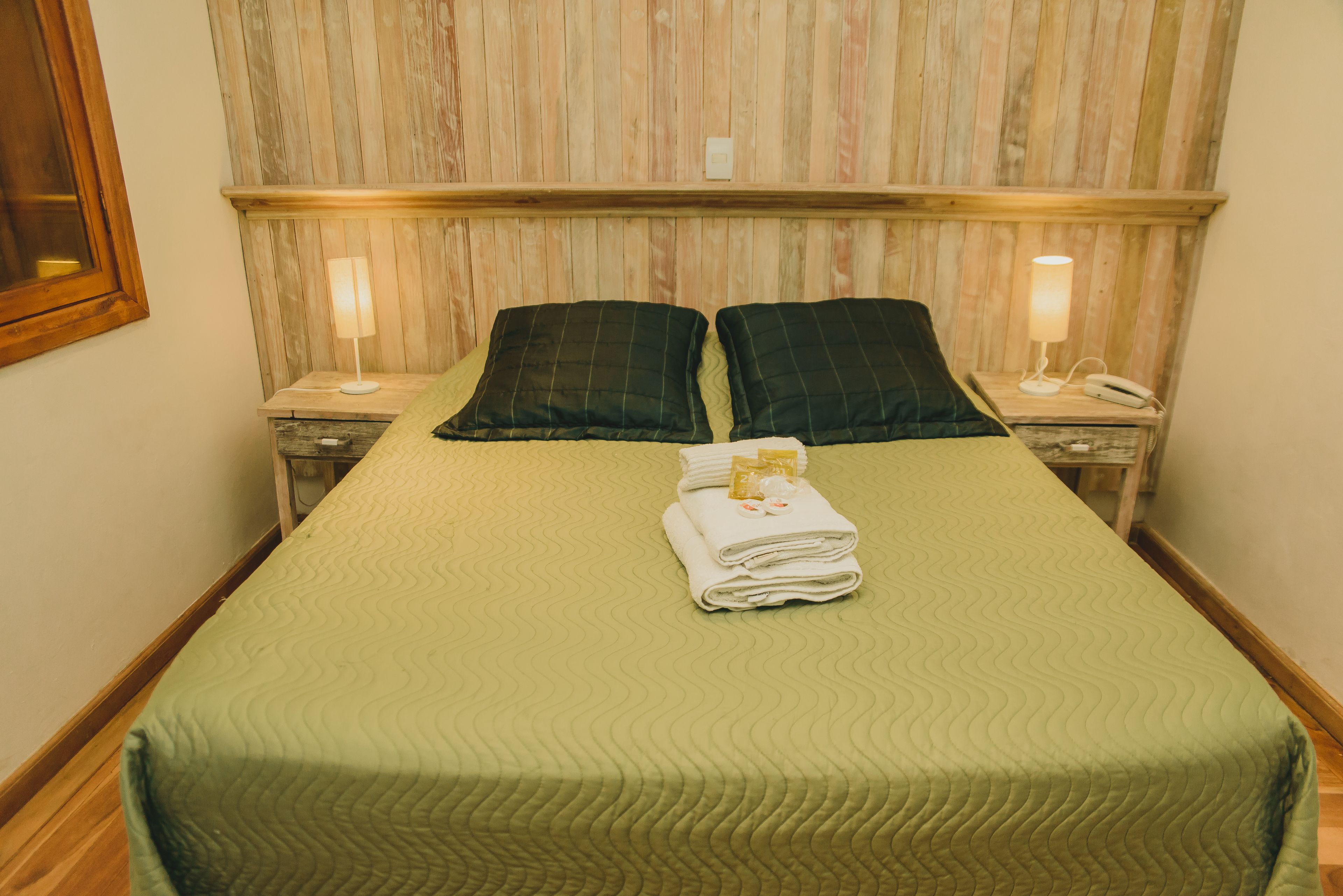 Une chambre d’hôtel avec un lit, deux tables de chevet, une lampe et une serviette pliée posée sur le lit.