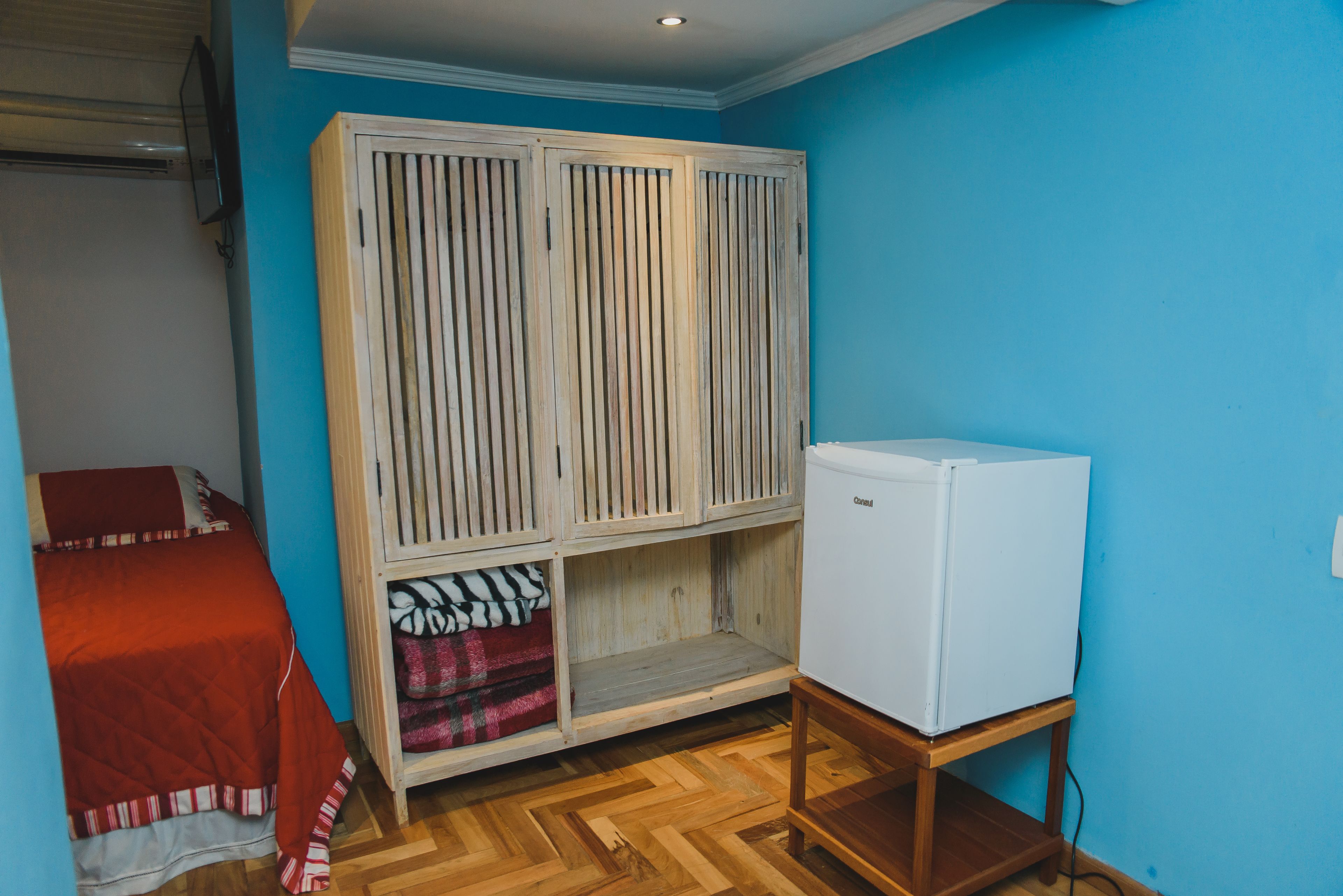 A bedroom with a bed, a wardrobe, and a refrigerator.