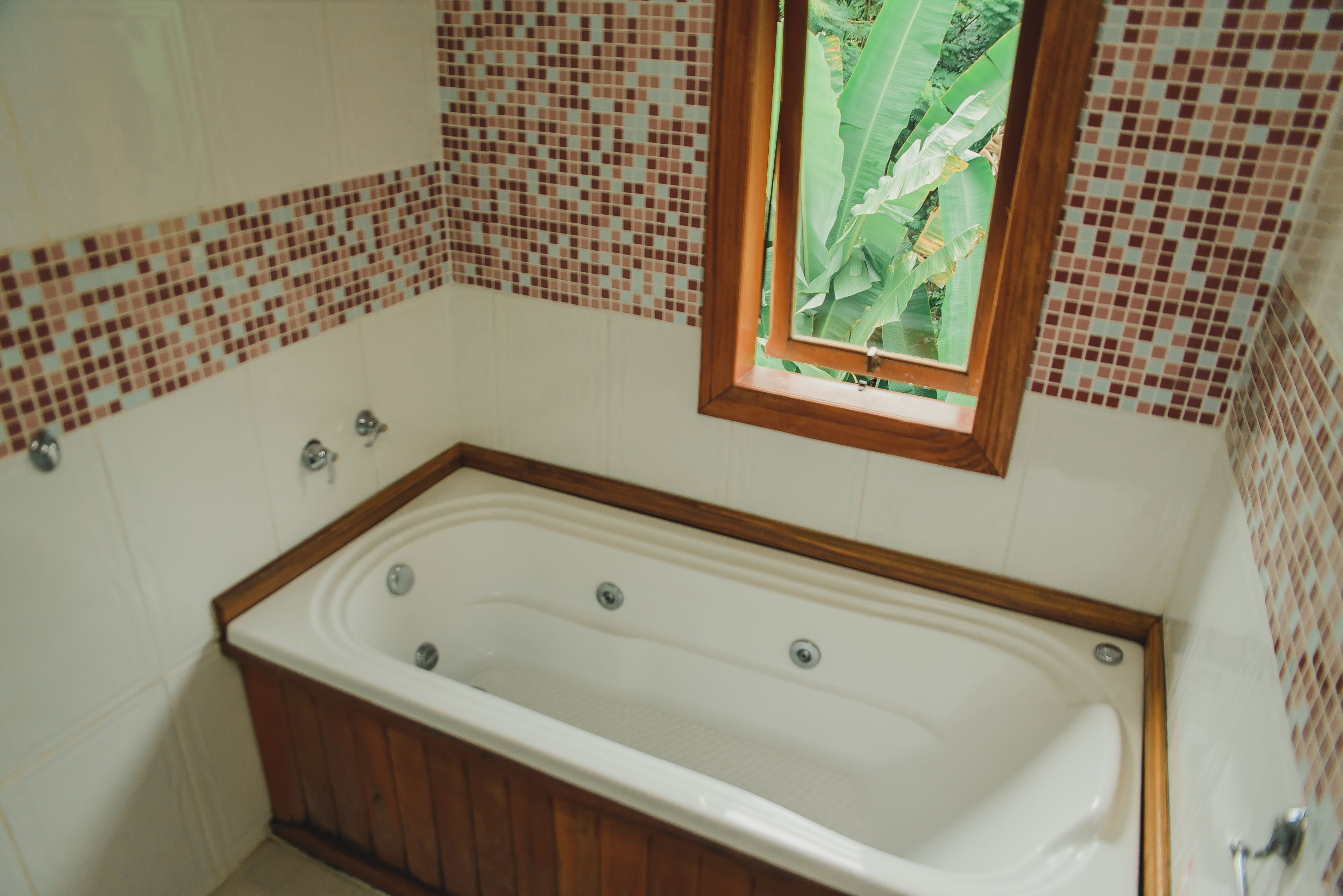 A bathroom with a freestanding bathtub, tiled walls, and a window with a view of greenery.