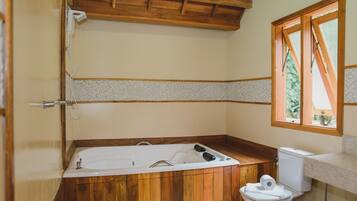 A bathroom with a wooden bathtub, a toilet, and a window with a view of trees.