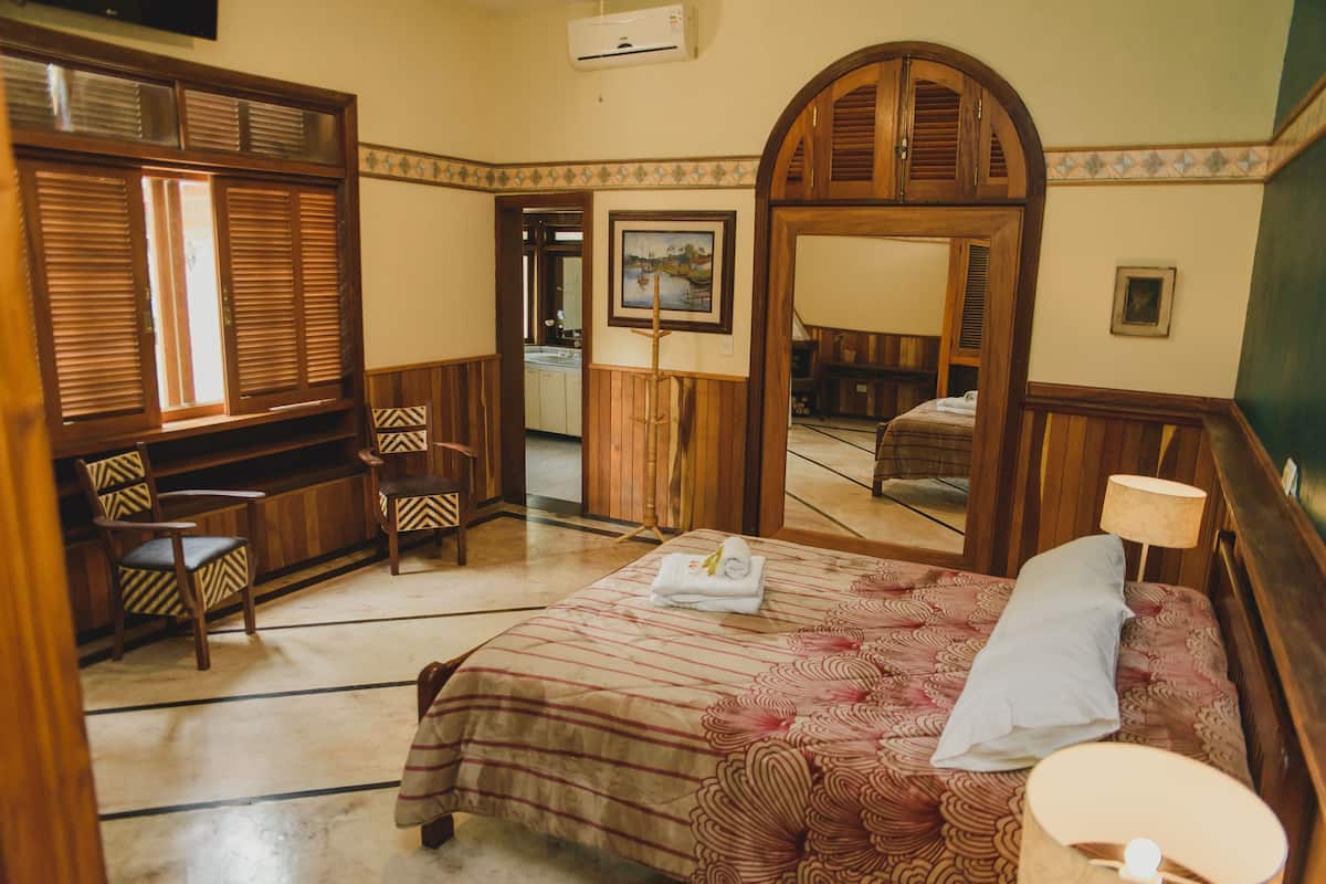 A hotel room with a bed, a desk, a chair, a mirror, and a window.