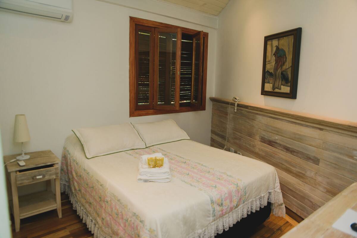 A neatly made bed with a floral bedspread, a wooden headboard, a nightstand with a lamp, and a painting on the wall.
