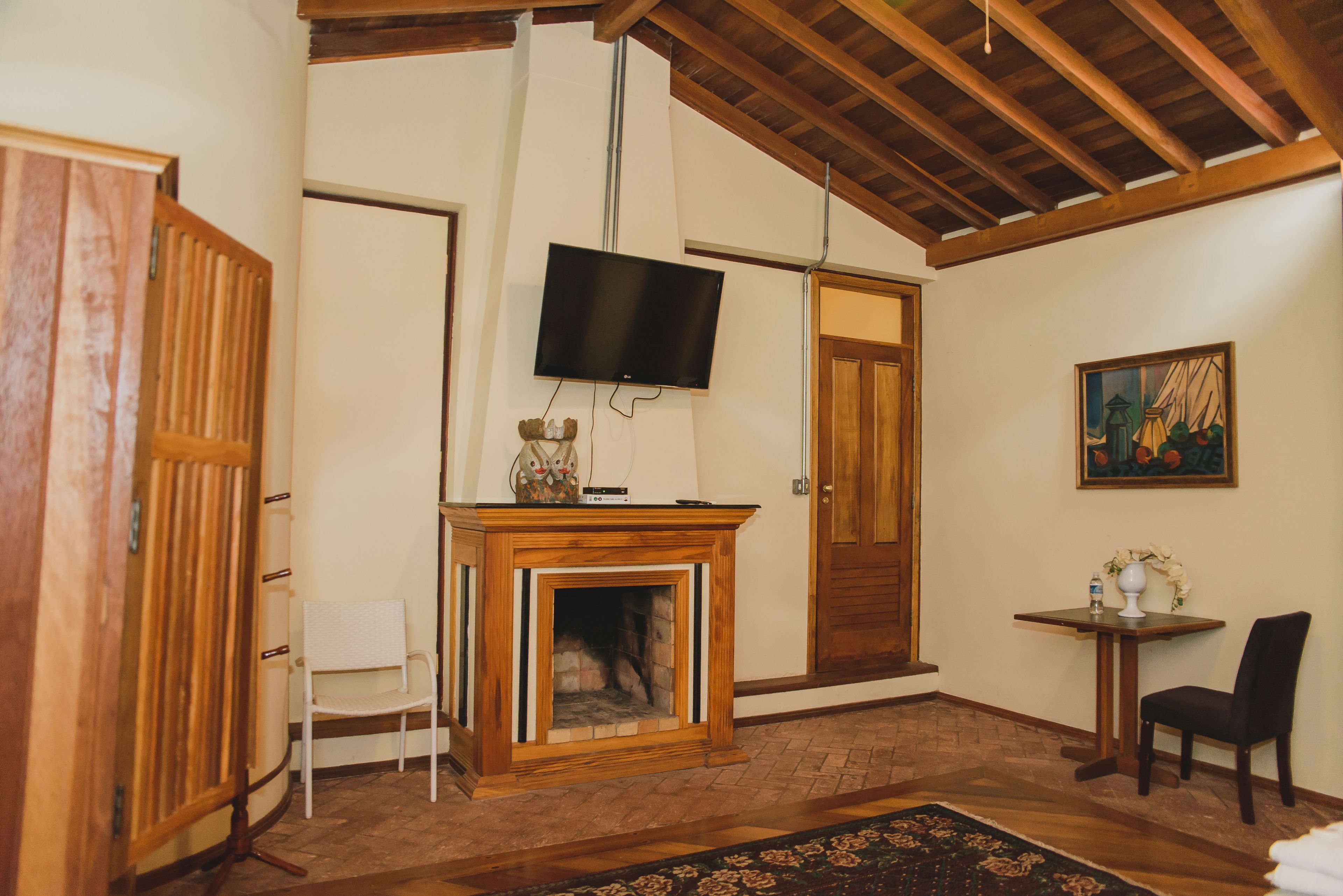 A living room with a fireplace, a television mounted on the wall, a wooden ceiling, and a painting on the wall.