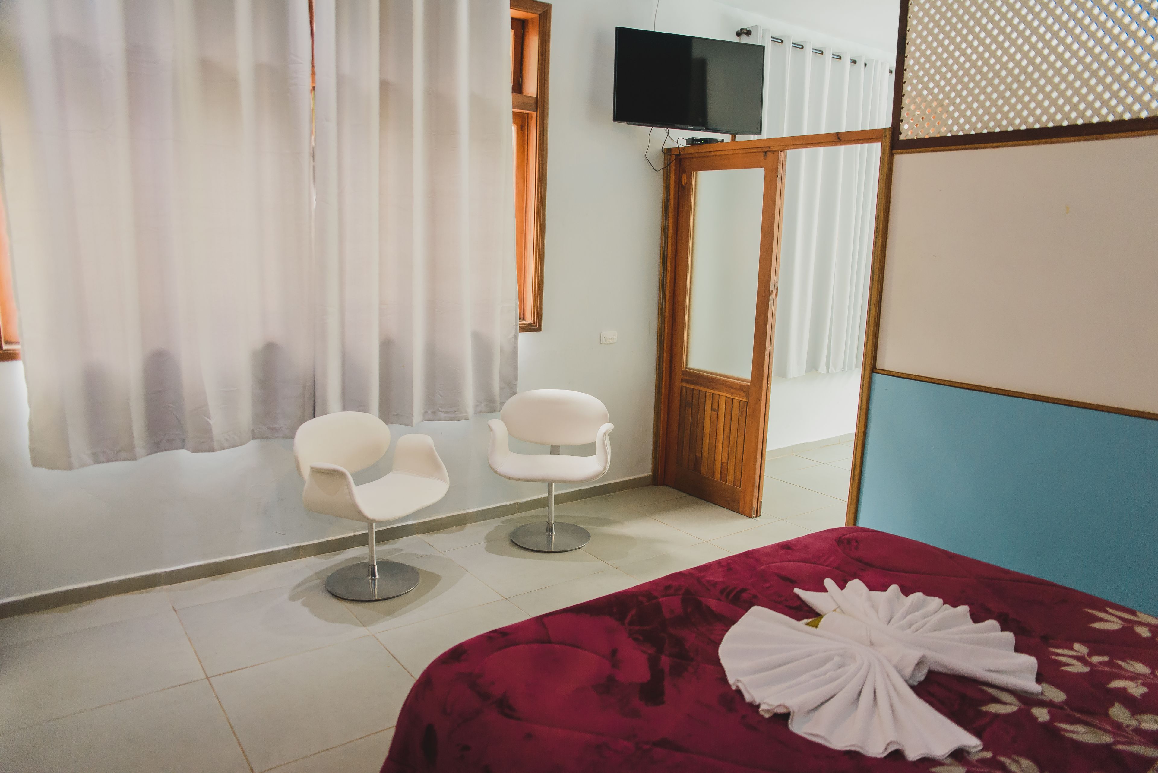 Hotellihuone, jossa on sänky, kaksi valkoista tuolia, televisio ja peili.