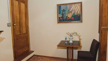 A hallway with a wooden door, a framed painting, a small table with a vase and flowers, and a chair.