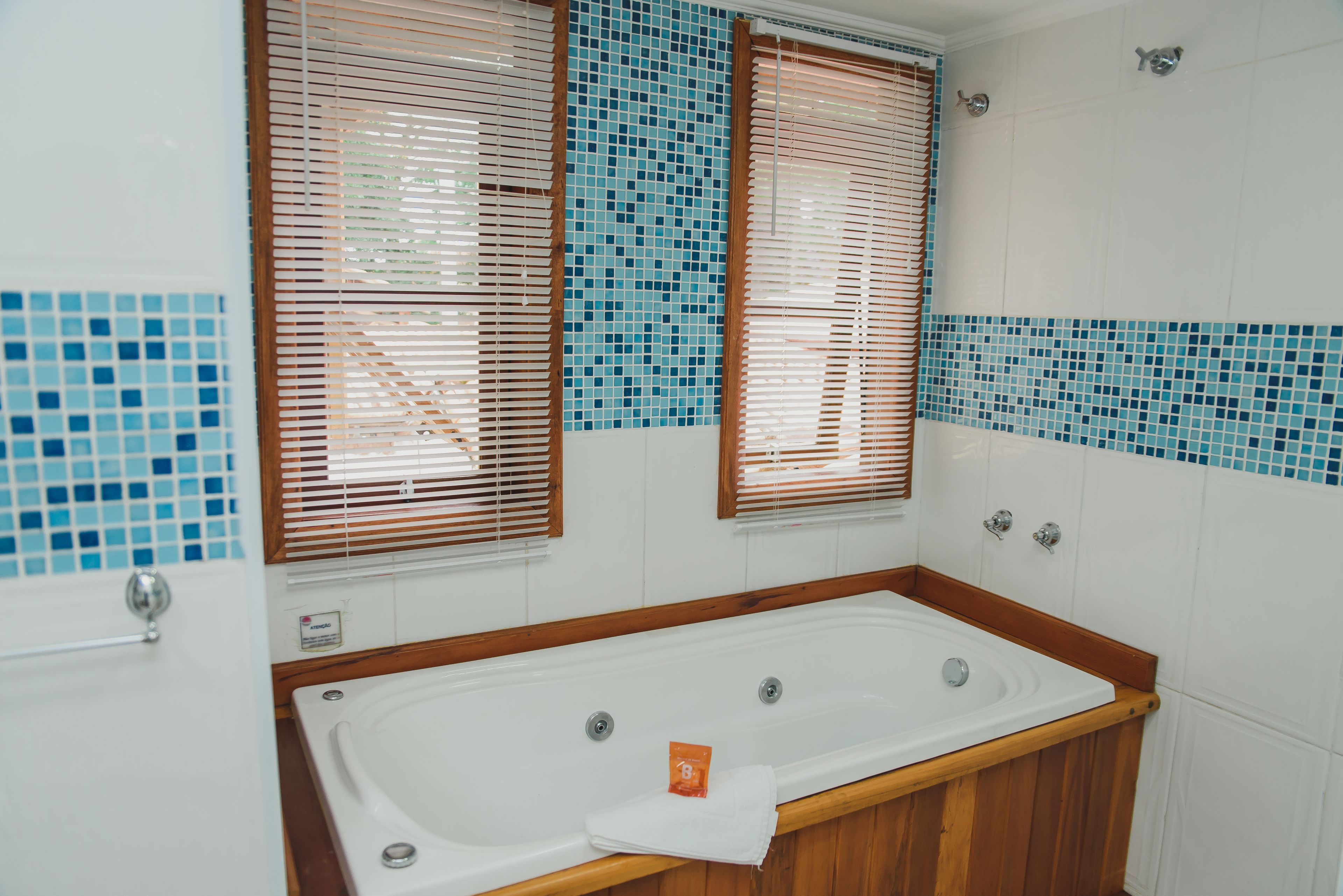 Une salle de bain avec une baignoire, des stores en bois et des murs recouverts de carreaux bleus.