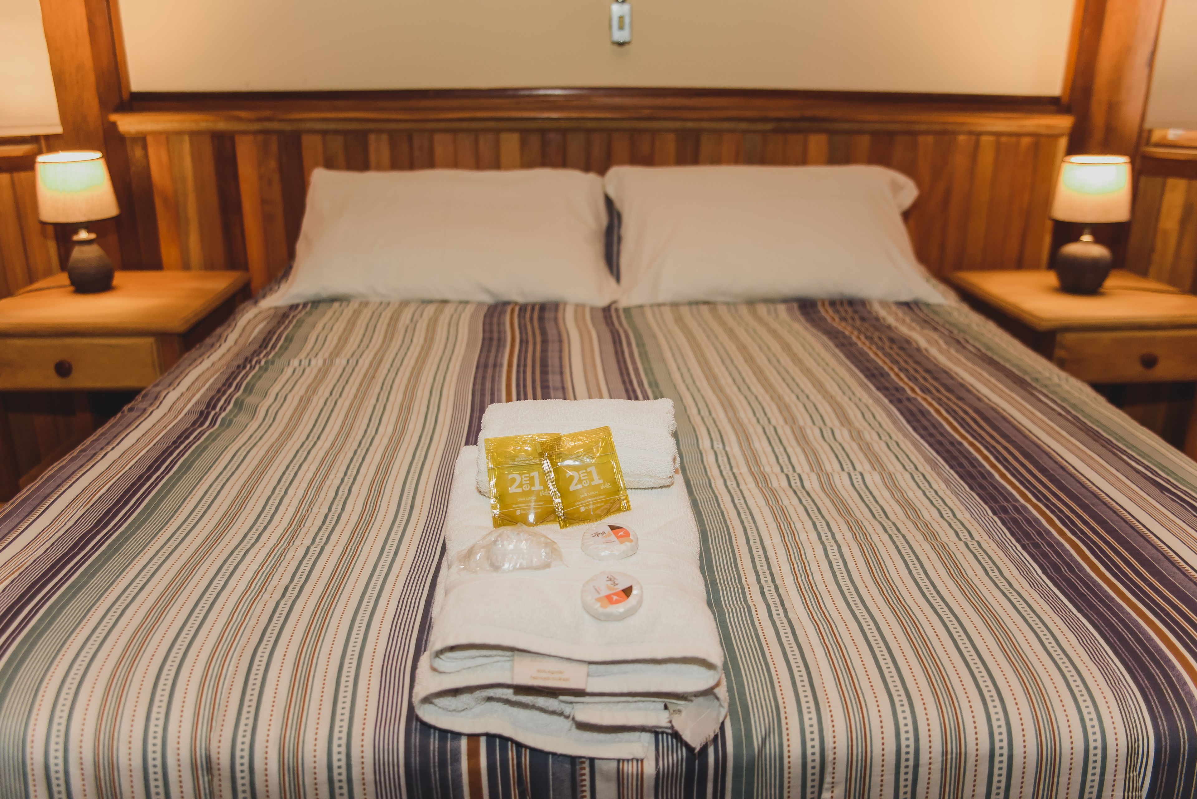 A neatly made bed with striped bedding, two pillows, and a towel with amenities.